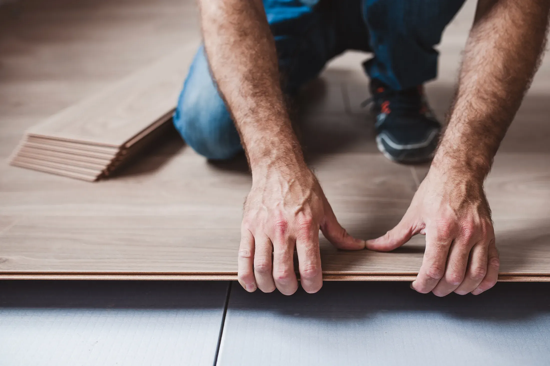 Hands pressing a click-lock vinyl plank into place next to a stack of planks